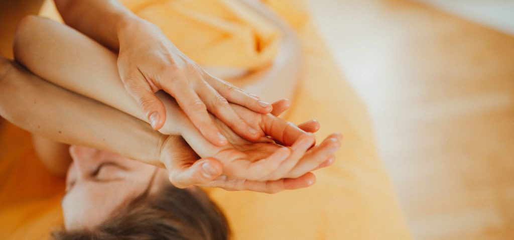 Massage, die Frau liegt entspannt auf dem Rücken, ihre Hand wird gehalten und liebevoll bewegt