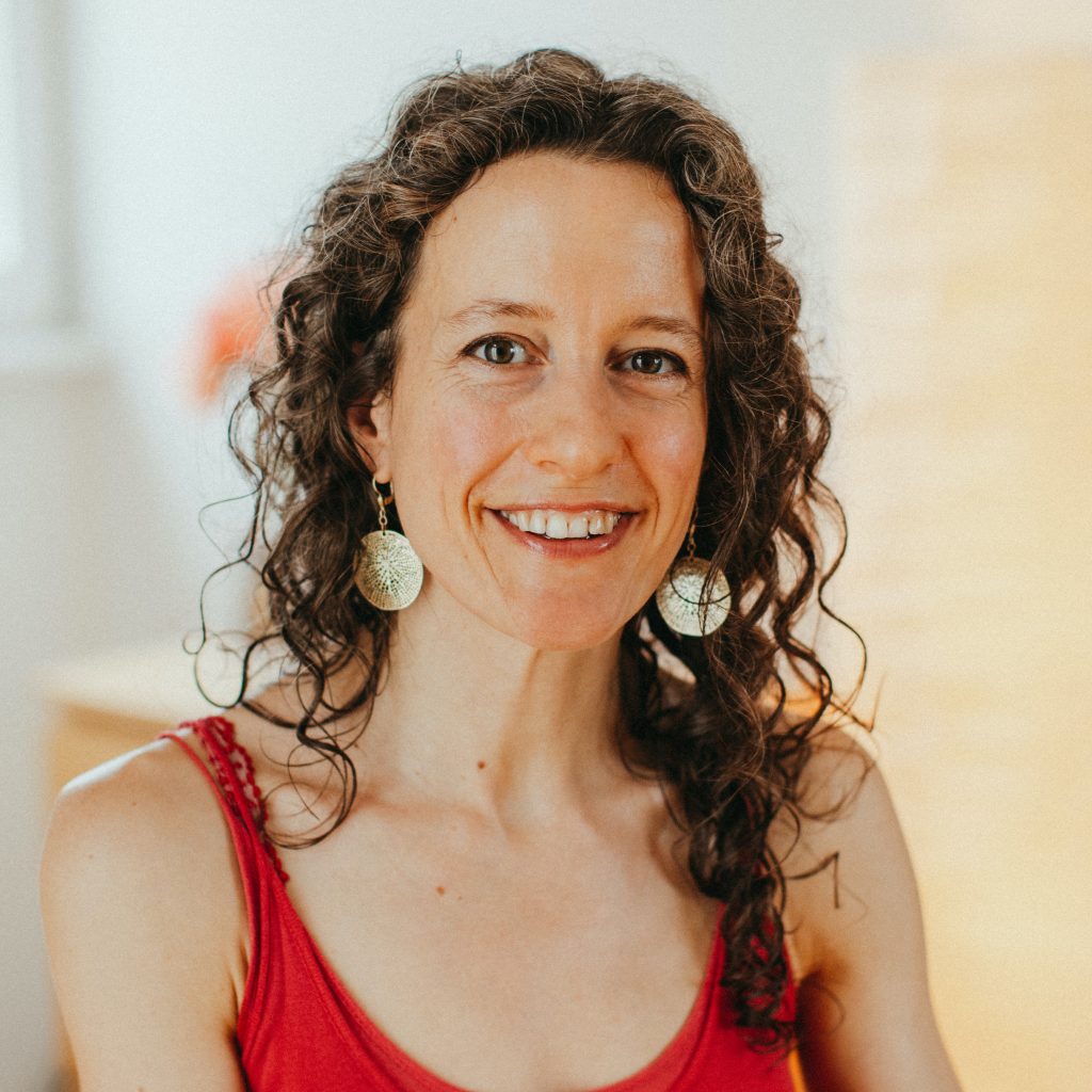 Achtsamkeitsbasiertes Coaching mit Melanie Ackermann. Frau Ackermann sitzt in ihrer Praxis in Tübingen und lächelt einladend und freundlich, um ihre Kundinnen willkommen zu heißen.